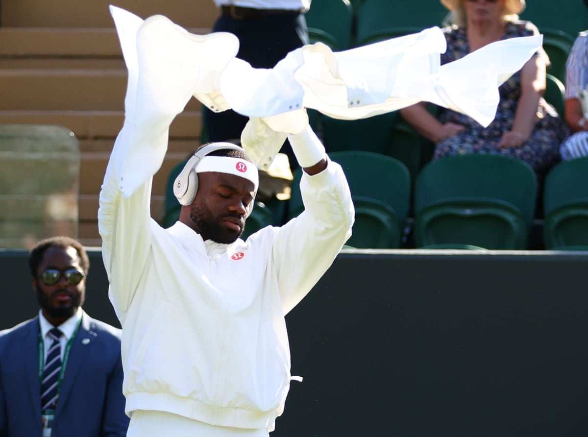 Tiafoe in headphones, arms aloft, holding white trousers