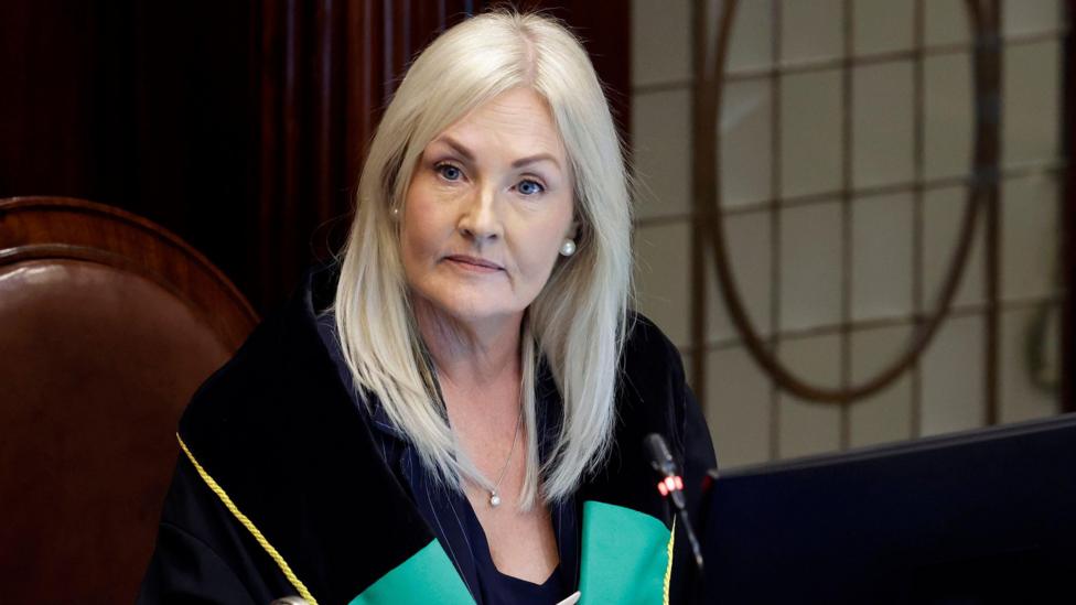 A woman with blonde hair wearing a green and black top