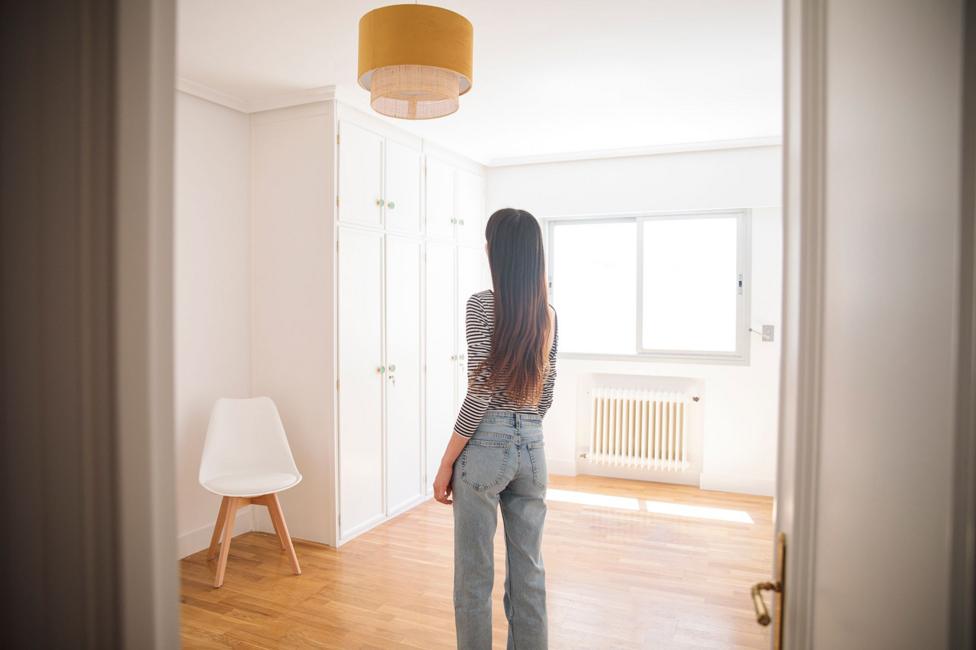 Young woman in an empty apartment looking around - stock photo