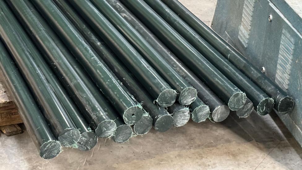 A pile of round black fence posts made out of a plastic-type material lie on factory floor.