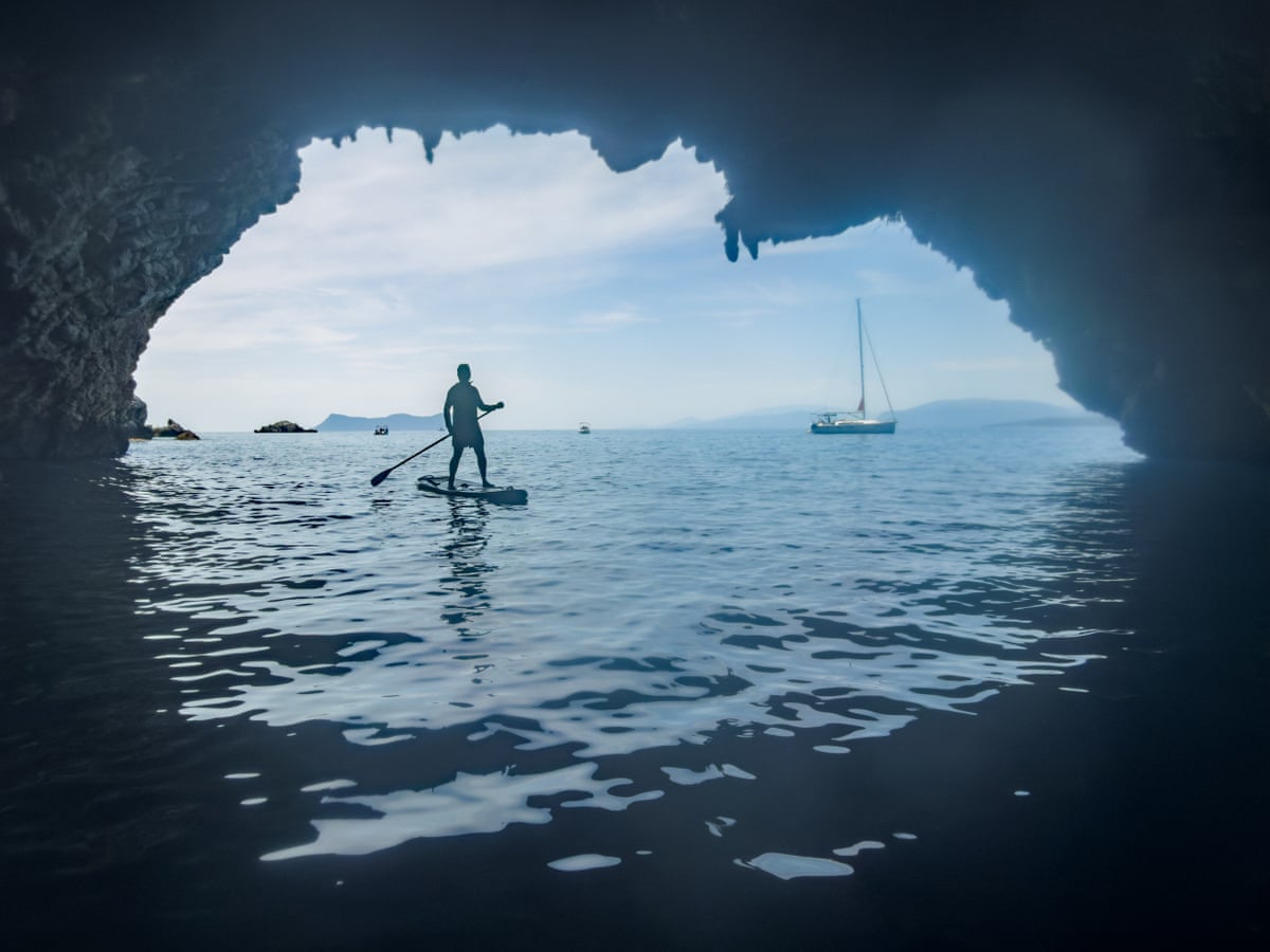 View of a man paddleboarding from the dark entrance of a sea cave