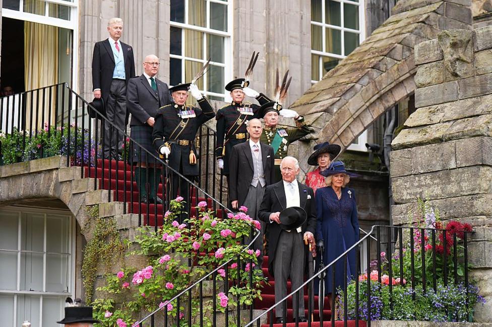 King Charles III, followed by Queen Camilla, Princess Anne, Princess Royal and Prince Edward, Duke of Edinburgh, walks down the steps at the Palace of Holyroodhouse in Edinburgh as they arrive to attend the Garden Party. John Swinney, in Highland dress, is with them. They are all dressed in morning wear.