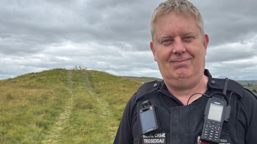 PC Dave Allen smiling at the camera in front of the burial mound