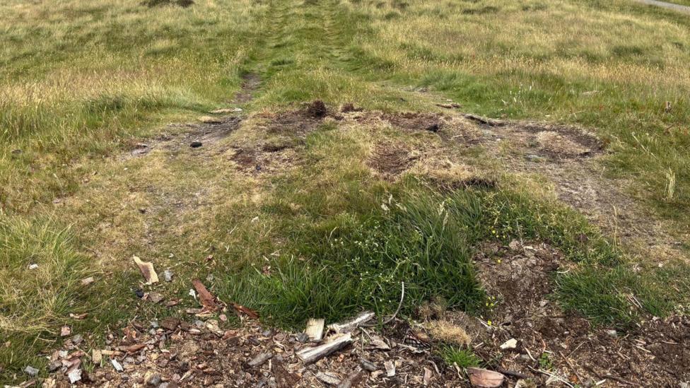 Grass has been worn away on the top of the mound where vehicles have driven