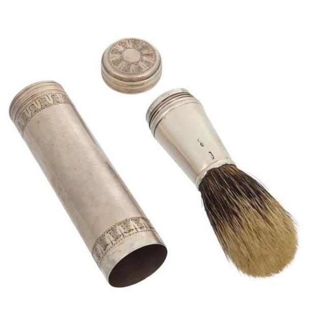 A silver cylinder with a lid and a silver shaving brush.