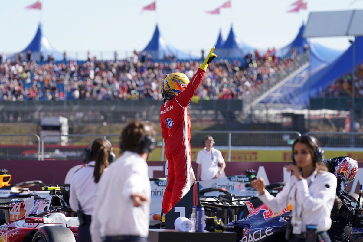 Lewis Hamilton stands on his car with his right arm raised