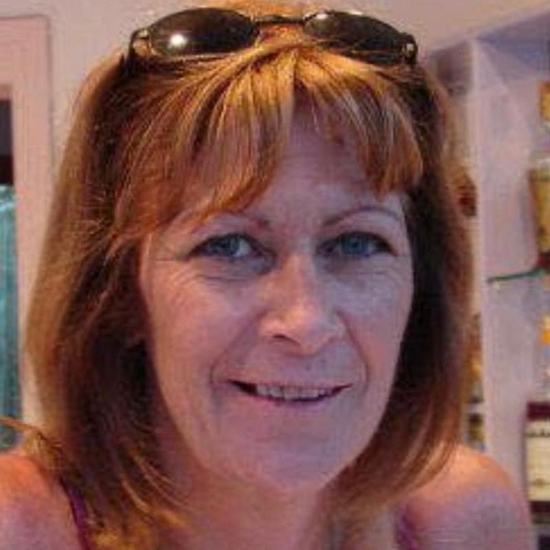 A woman with shoulder length hair and sunglasses perched on her head, smiles at the camera