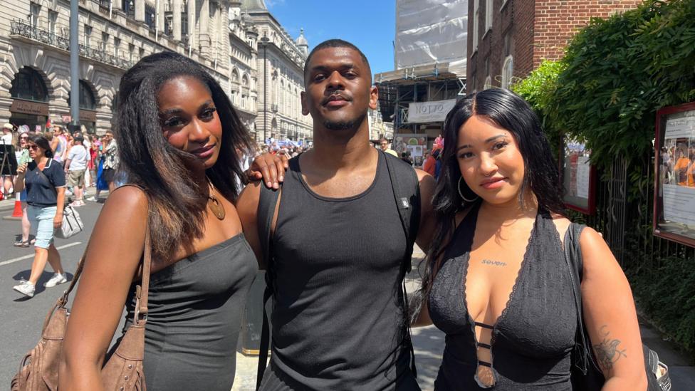 Three friends - with Besa Nolan in the centre - posing together on a sunlit London street during the event, all dressed in matching dark outfits.