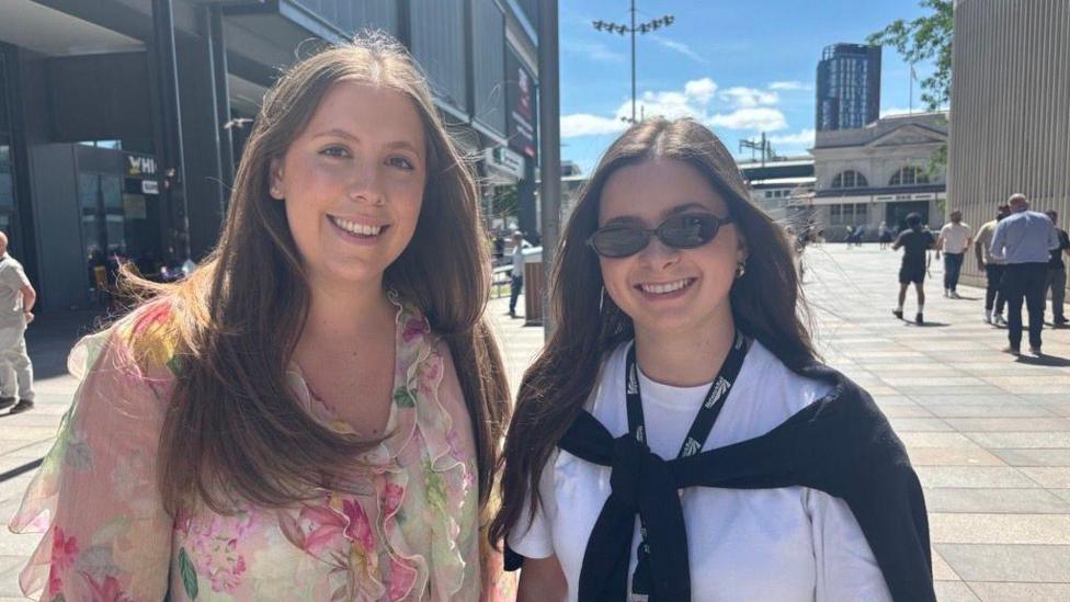 Two women standing in Cardiff city centre. On the left, she is wearing a florar pink top.