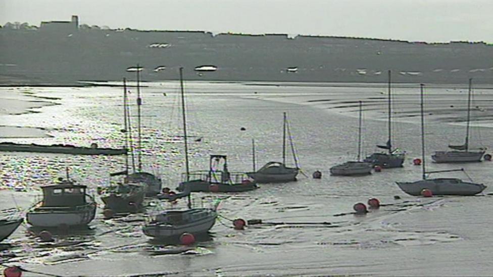 The image shows several boats moored in the mudflats of Cardiff Bay before the barrage was built. The Penarth headland can be seen in the background.