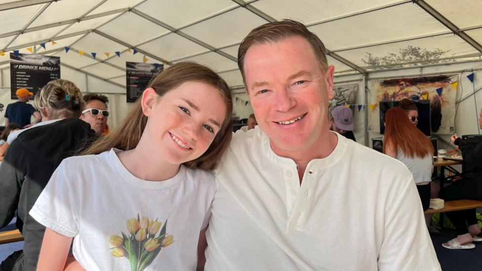 A young girl and her father sat a table inside a marquee.