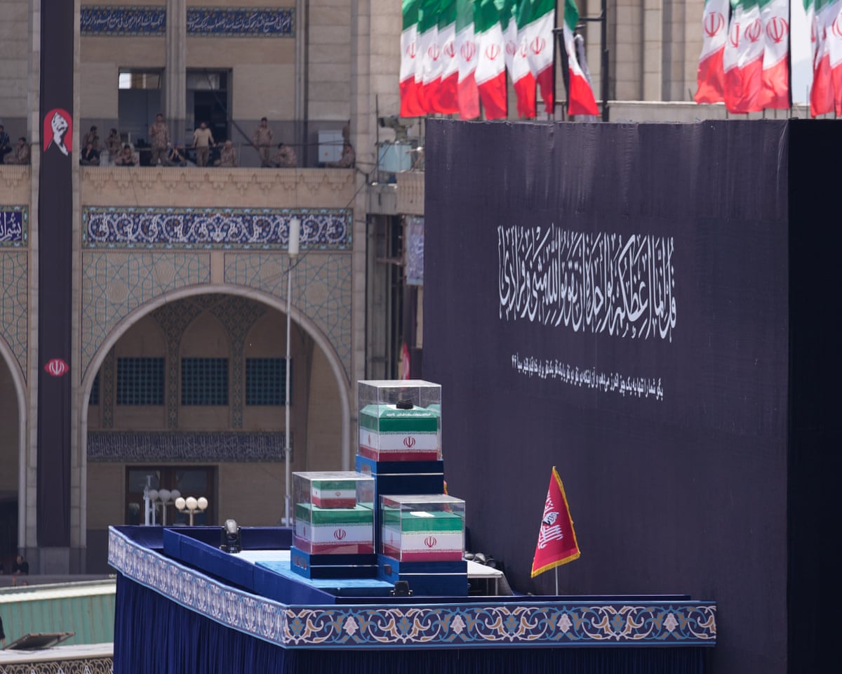 Three coffins in glass cases, draped in the Iranian flag, on a tall platform