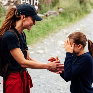 Kate looks at Charlotte who covers her face while a boy plays with a dog in the background