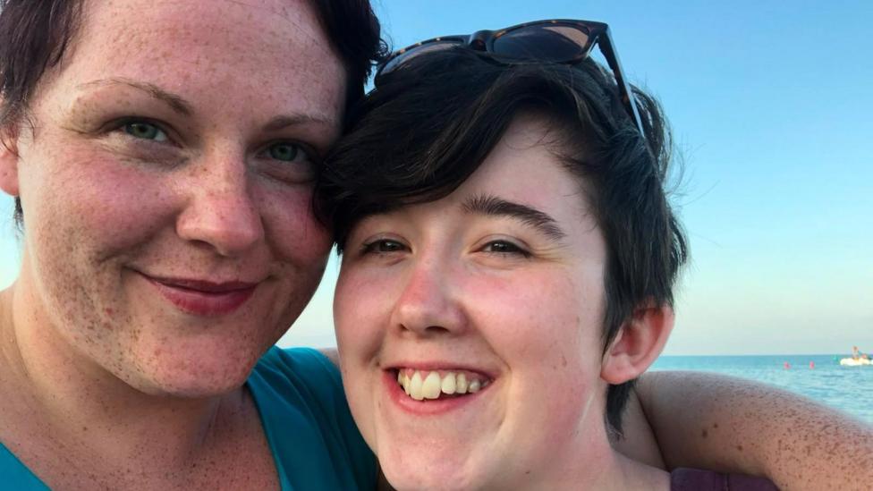 Sara Canning. left and Lyra McKee, right, pose for a selfie. They are close to the camera and the sea is in the background.