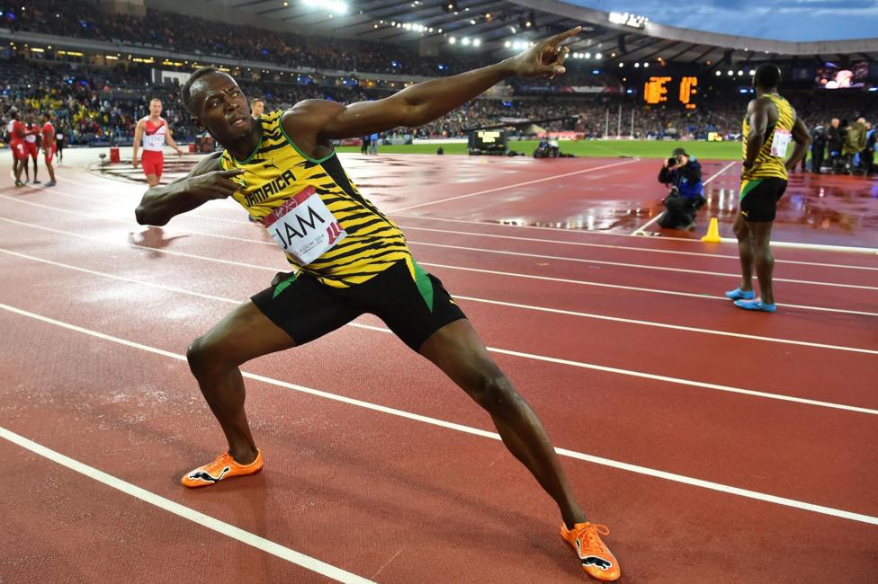Usain Bolt is wearing colourful yellow, black and green running kit while striking a pose on a running track.