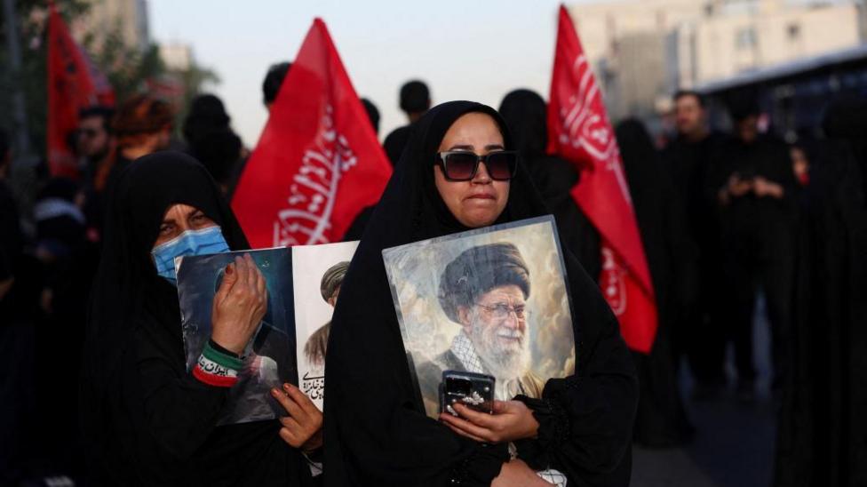 woman holds photo of Khamenei with red flags in the background
