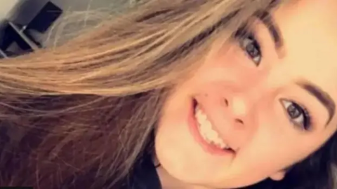 Emily Moore selfie. She is smiling at camera. She has long brown hair. The picture is taken at an angle so the top of her head is in the top right hand corner while her hair falls towards the bottom. She looks genuinely happy.