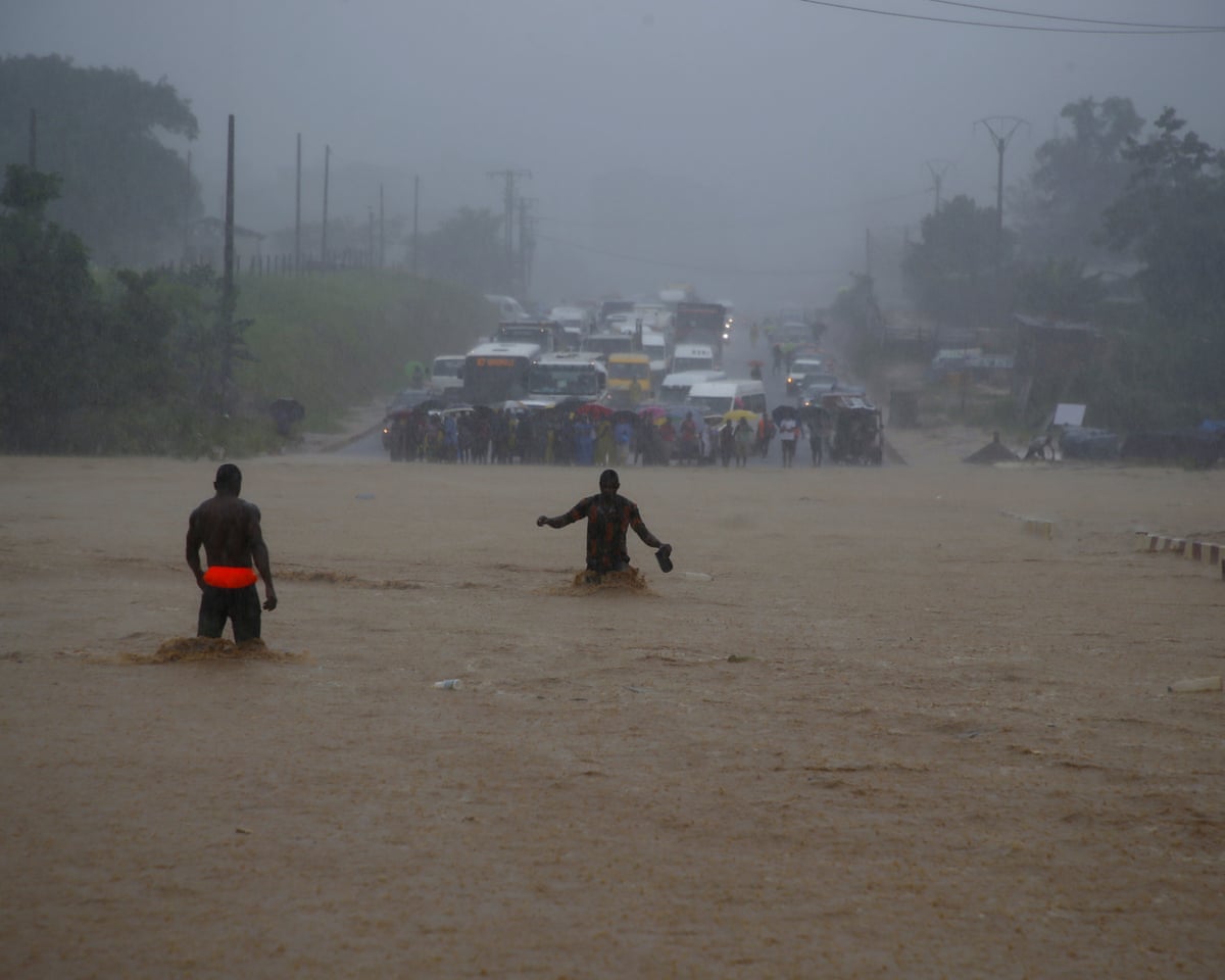 People wading waist deep across what looks like muddy river towards halted rows of cars