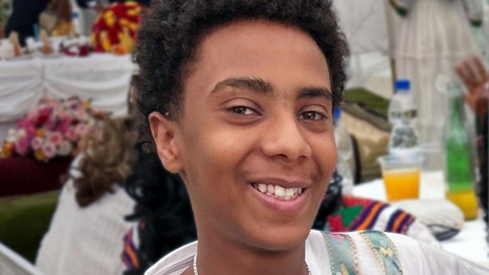 A young boy with short dark curly hair smiling at the camera.