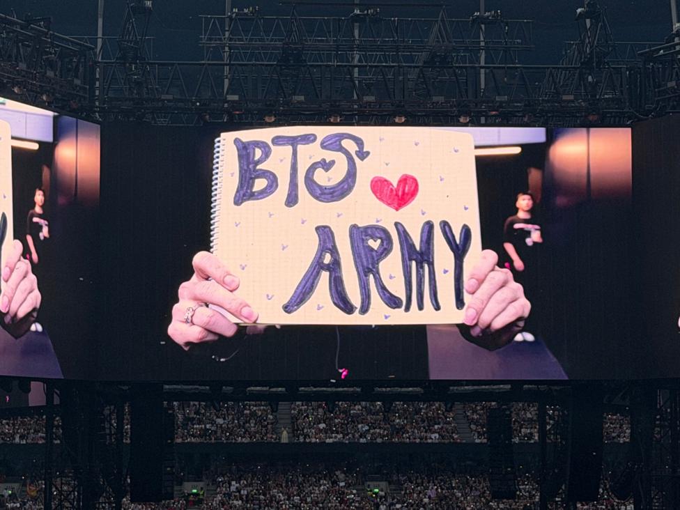 Jin from BTS holds up a hand-written sign saying