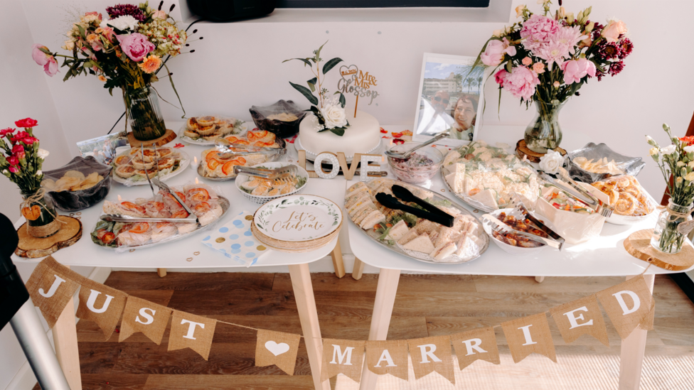 A table filled with food and flowers with a sign which reads Just Married