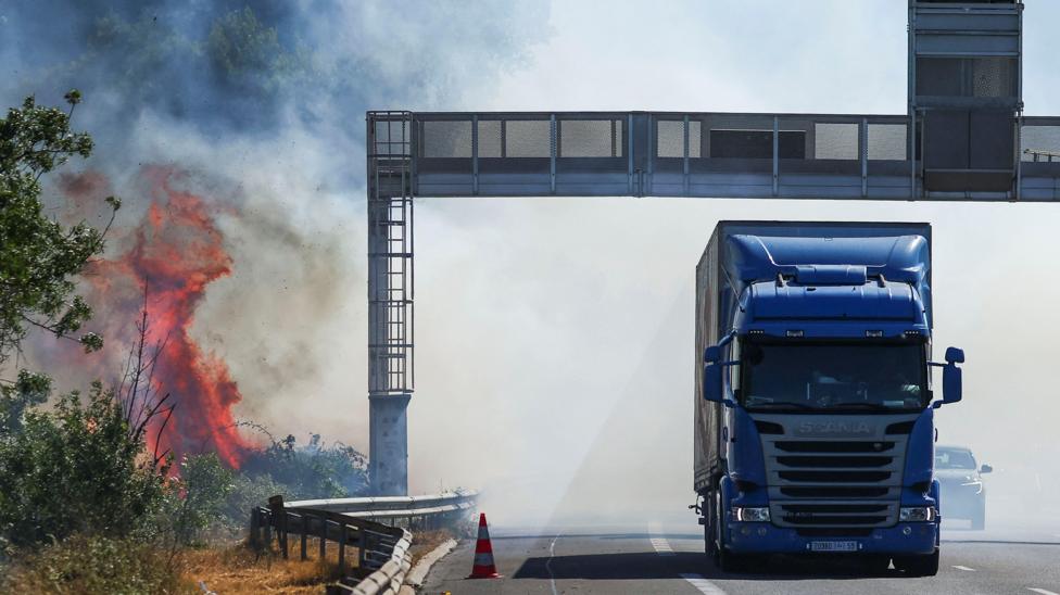 A truck drives next to a fire as a firefighting plane (not pictured) flies to battle wildfire near the A9 motorway near Beziers, France, July 3, 2026.