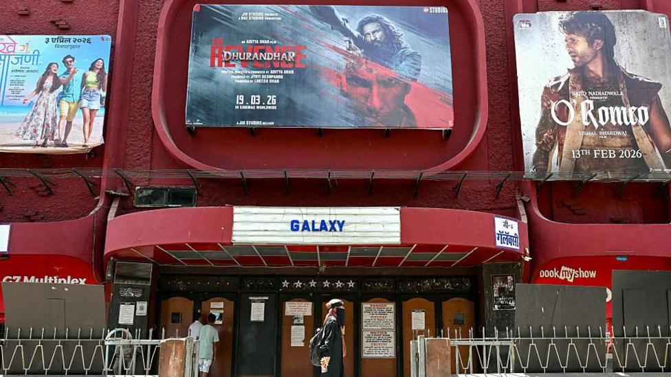 A woman walks past a poster of Indian Hindi-language spy action thriller film Dhurandhar: The Revenge (C), displayed outside a cinema hall in Mumbai on April 7, 2026.