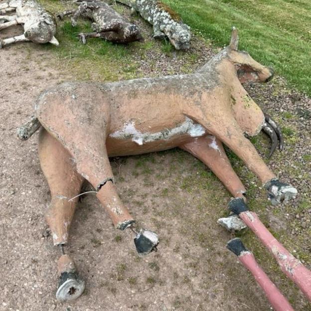 A concrete cow lying on its side with cracks in its legs