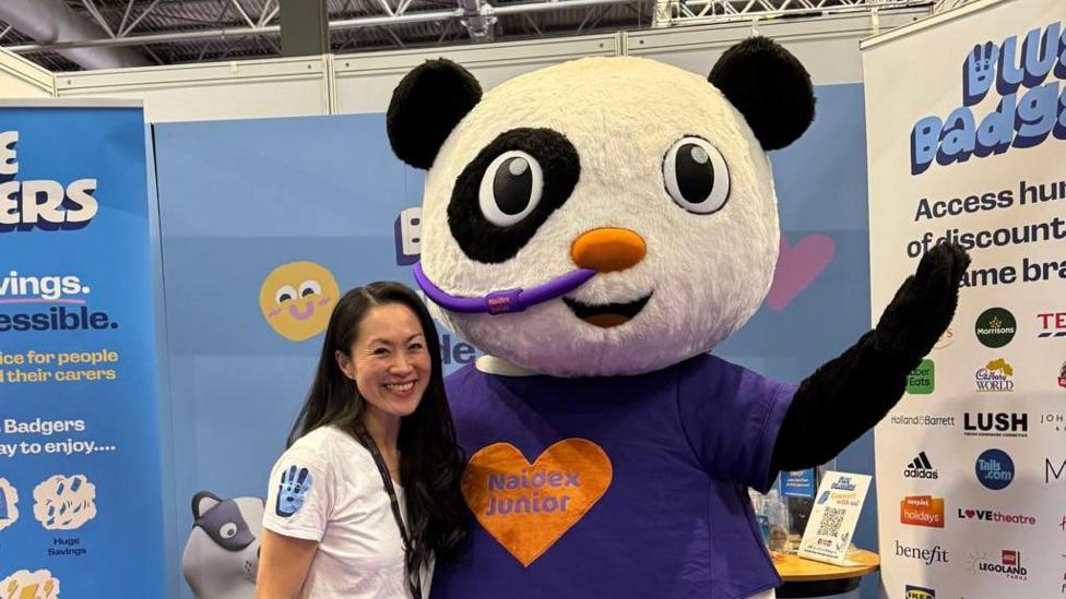 A woman stands with a panda mascot and a convention.
