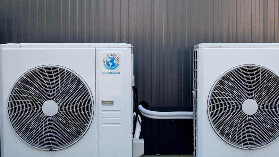 Two brilliant white air conditioning units sit alongside each other outside a building. The only thing you see behind them are the corrugated steel oanels of the building itself.