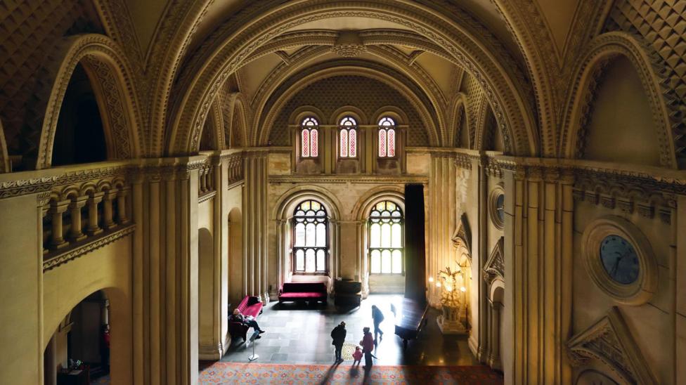 The Gothic grand hall at Penrhyn. The double height room has elaborate arched ceilings, large stained glass windows and large circular clocks carved into the stone