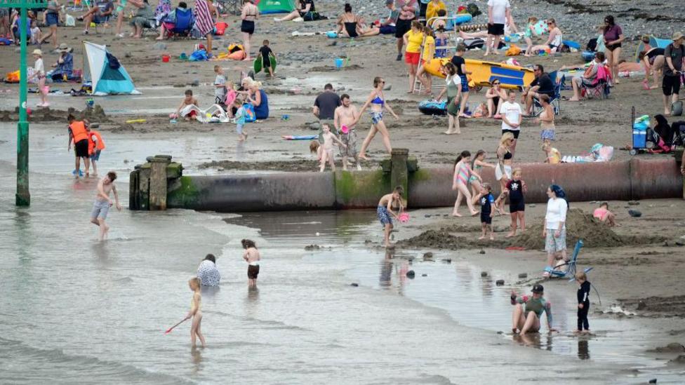 Plant yn chwarae wrth bibell gwastraff dwr ar draeth y Borth yng Ngheredigion
