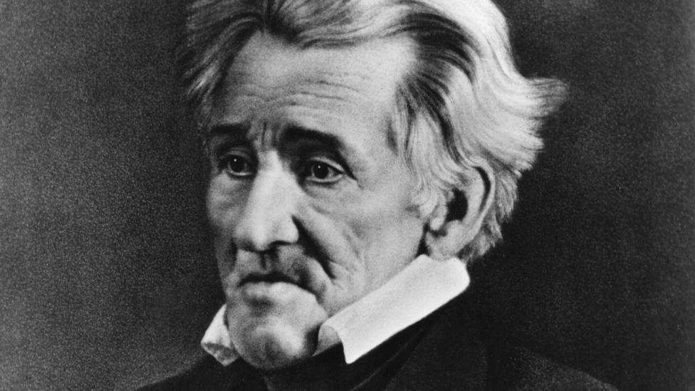 A black and white archive image of US President Andrew Jackson. He had short, wavy grey hair and is wearing a black suit and a white shirt with a high collar.