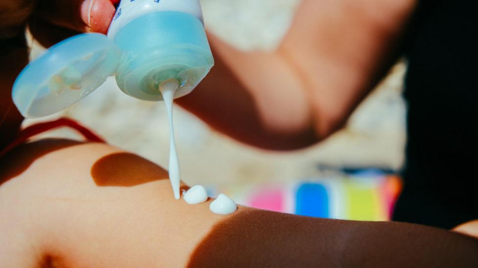 Woman putting suntan lotion on her child at a sunny day in summer vacation.