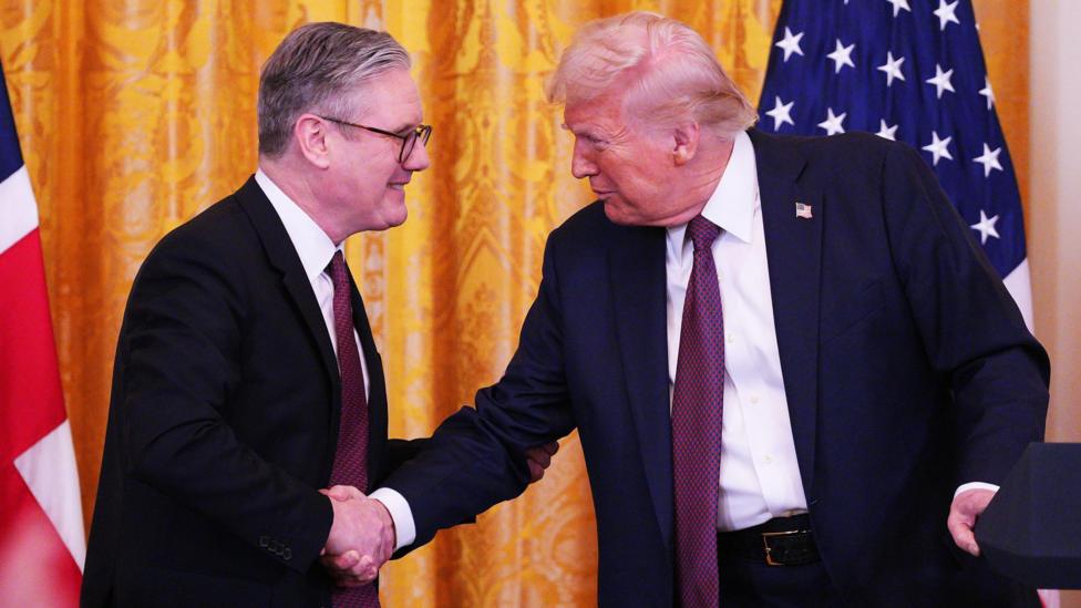 US President Donald Trump and Prime Minister Sir Keir Starmer shake hands during a press conference at the White House in February 2025. Behind them is a yellow curtain behind a Union Jack and US flag.