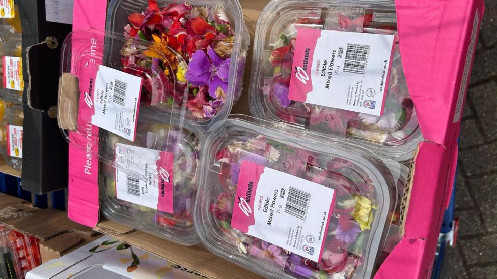 A number of boxed edible mixed flowers, piled up in a pink cardboard box.