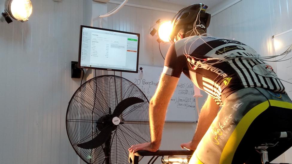 A cyclist on a static bike undergoes a test, with cables running from his helmet and shirt.