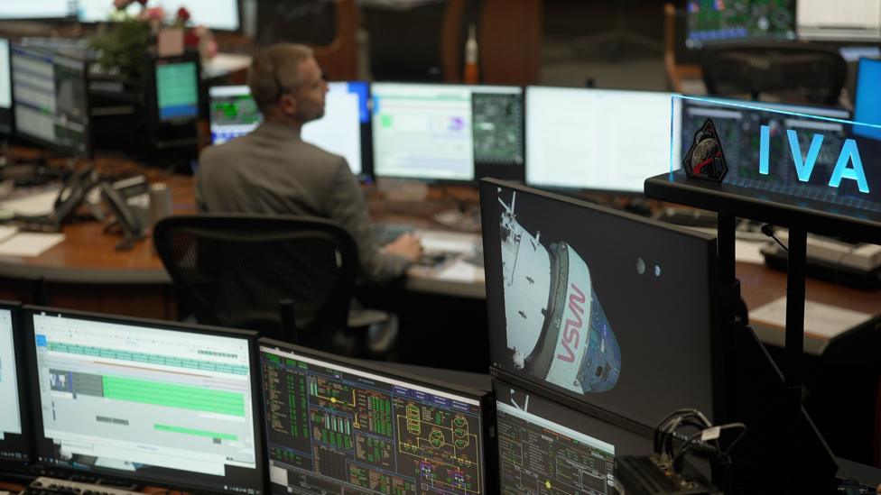 Mission control at the Johnson Space Center in Houston. Rows of computer screens with one worker sitting at their desk. 