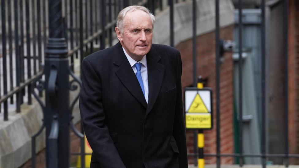 Paul Dacre, wearing a black coat, white shirt and blue tie, arrives at the Royal Courts Of Justice