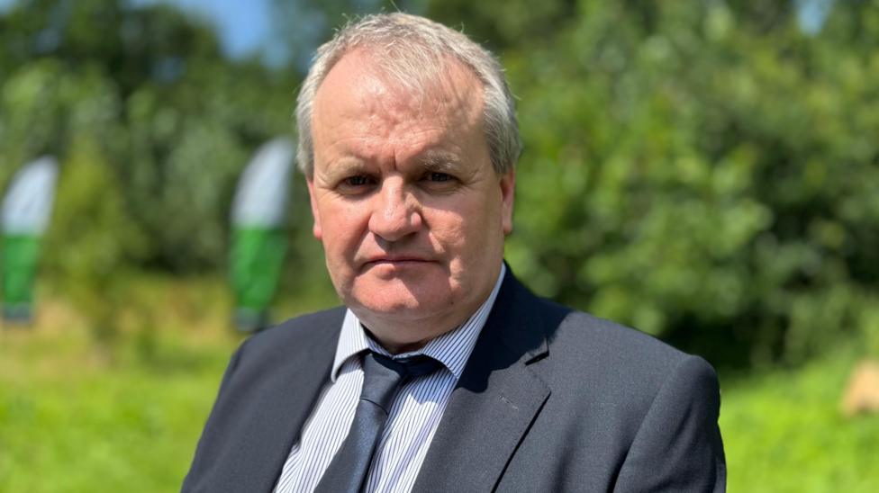 Nigel Manley has short grey hair and is wearing a white striped shirt, black blazer and black tie.
