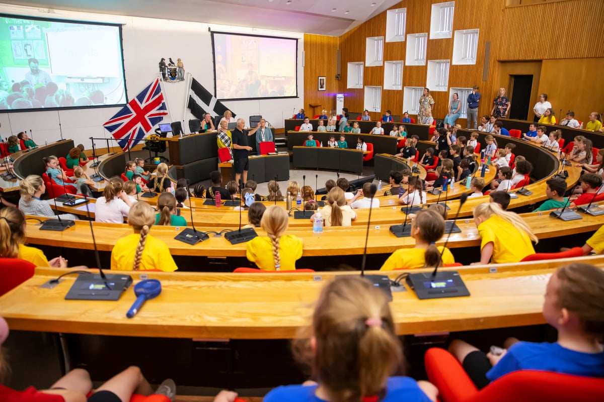 Children seated at Truro county hall with union jack and Cornish flags on display.