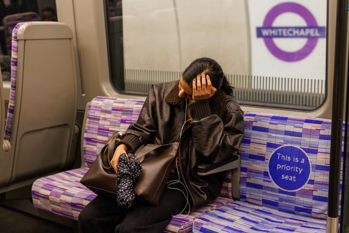 Tired woman rests her head in her hand on the Elizabeth line tube.