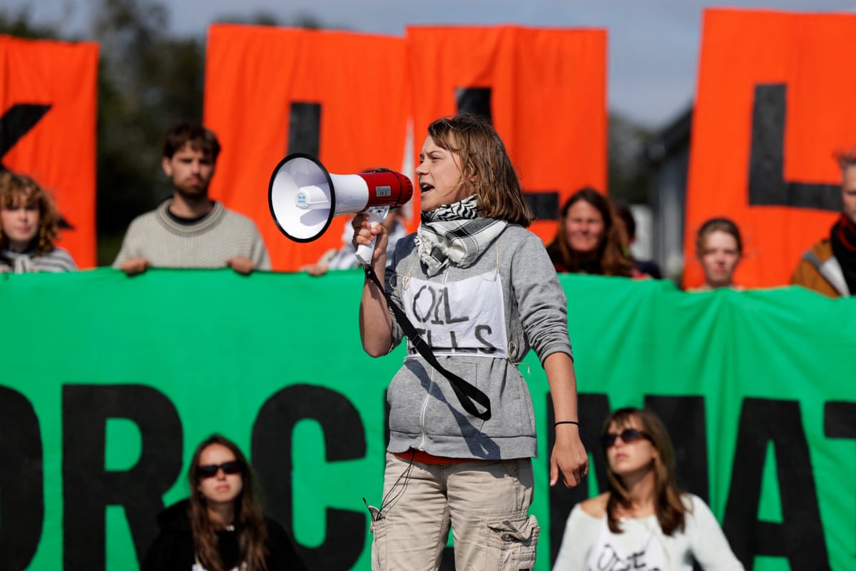 Greta Thunberg speaking through a megaphone wearing a sign that reads ‘Oil kills’