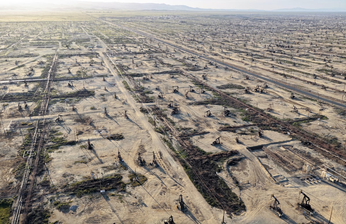 An aerial photo showing large dusty field filled with oil pumpjacks stretching into the distance