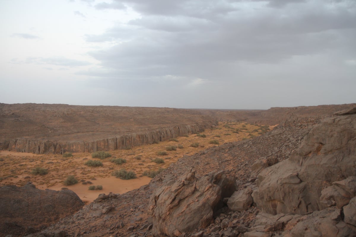 A shot from high up showing a rocky red and brown landscape with sparse, scrubby vegetation