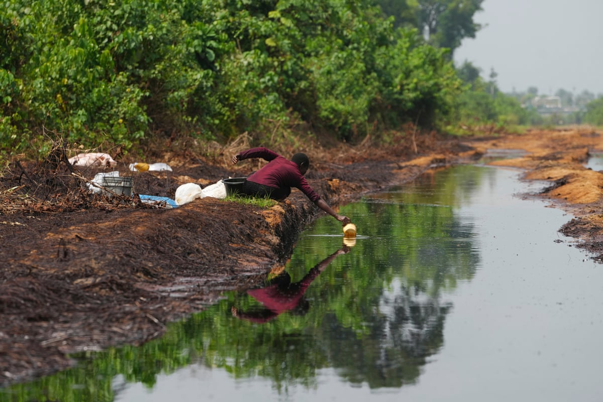 A woman crouches at the side of a body of water to dip a large cup into it