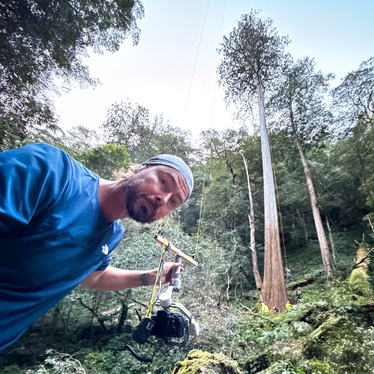 A man holding a piece of photographic equipment attached to two yellow ropes looks at the camera