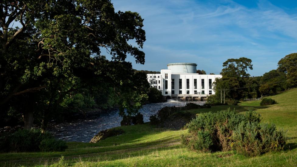 The white art deco power station at Tongland next to a river and among trees and fields