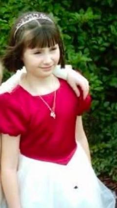 A girl with short dark hair wears a prom-style dress with a satin pink top half and a white tulle skirt.