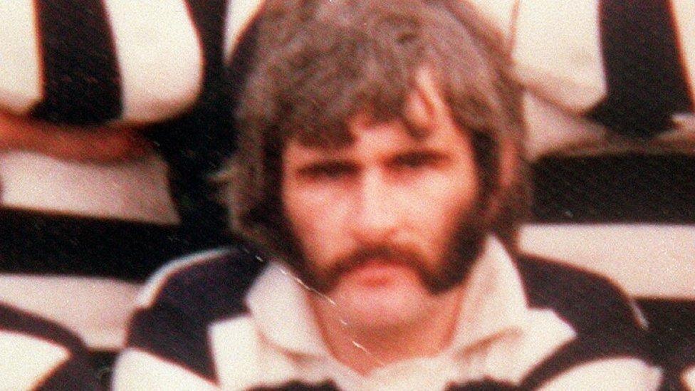 A blurred image of a man with a moustache and a black and white stripped polo short
